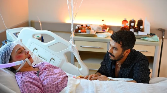 Woman in a hospital bed wearing an oxygen mask, resting as a man sits beside her and holds her hand.
