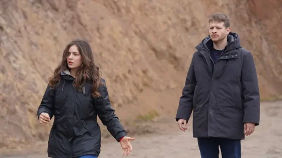 Two adults in dark jackets walk along a rocky dirt path with a steep earth wall in the background.
