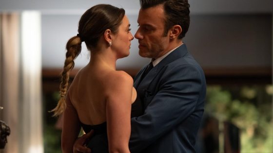 Couple dancing closely indoors: woman in a black strapless dress with a braided ponytail and a man in a blue suit gaze at each other.