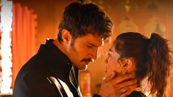 A man gently holds a woman's chin, leaning in with a tense expression in a warmly lit room.