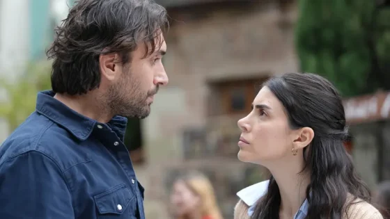 Two adults stand close and face each other with serious expressions outdoors, suggesting a tense conversation.