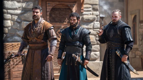 Three men in medieval armor stand with swords in a stone courtyard.