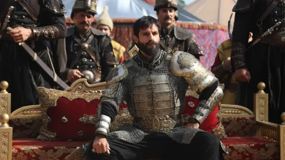 Bearded man in ornate plate armor seated on a red throne, flanked by armored guards in a ceremonial setting.