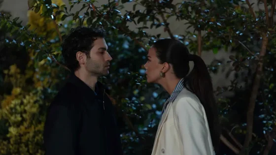 Two people stand close together at night in a garden, facing each other as if about to kiss or share a moment.