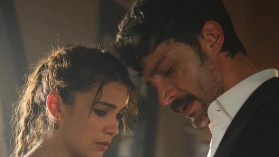 A man and woman lean close together, both looking down with somber expressions.