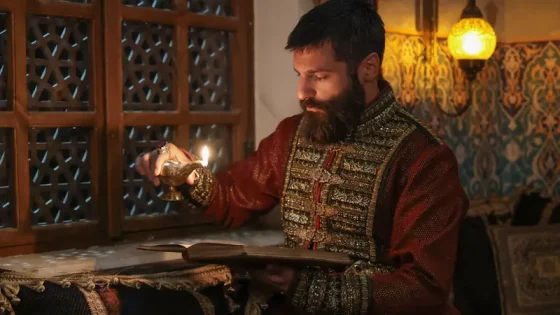 Bearded man in ornate historical clothing lighting a candle beside an open book by a wooden lattice window.