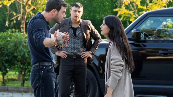 Three people: a man in a navy shirt gesturing with a tied cloth, a woman facing him, and another man standing near a black SUV in a driveway or parking area.