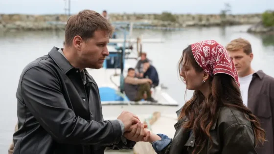 Two people shake hands on a dock by a small boat, with others in the background.