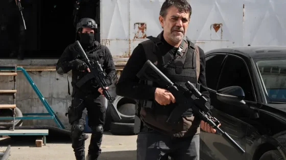 Two men in tactical gear with rifles standing outside a building beside a black car, one in front and another masked man behind them.
