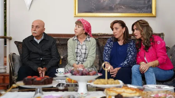 Four people sit on a sofa around a table of assorted desserts, chatting indoors.